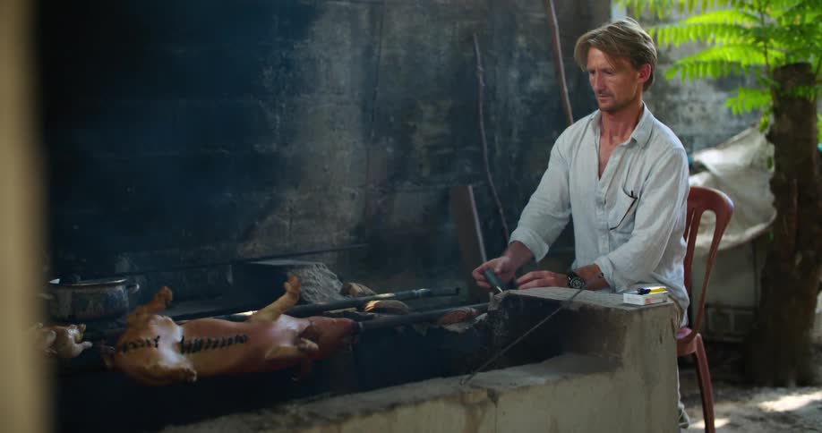 A man turns a pig on a roast on an outdoor smoker