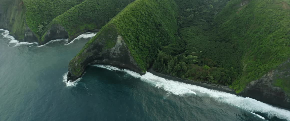 Wave crash against a coastline containing many vegetation covered hills and mountains