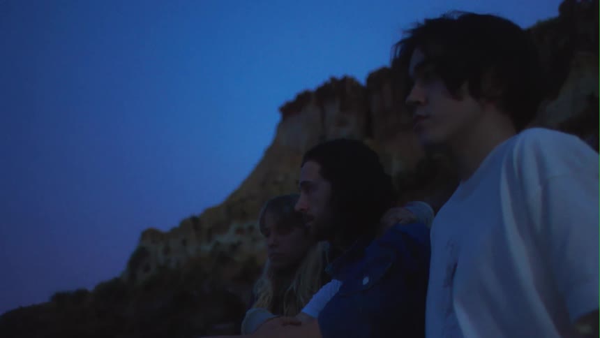 A woman sits on a beach with her arm around her husband who sits beside their son