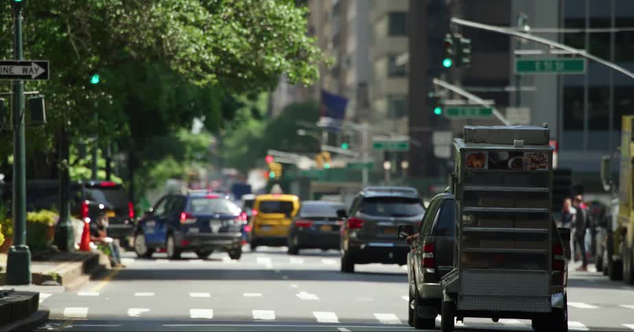 Vehicles driving down a city street with a few pedestrians