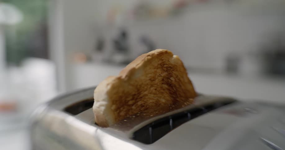A piece of toast pops out of a stainless steel toaster