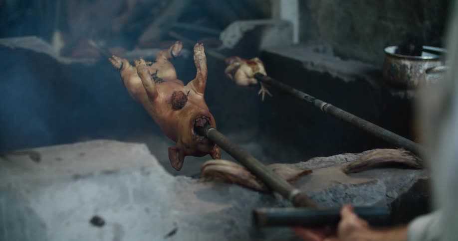 A man turns pigs on a spit on a smoker