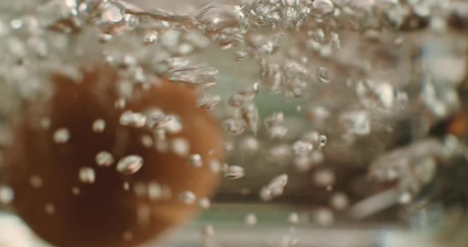 A metal spoon places an egg into water boiling in a glass pot