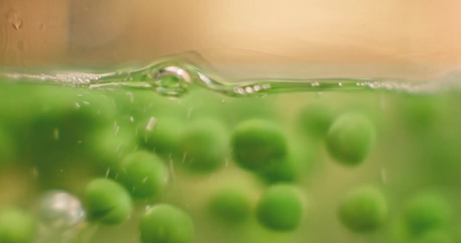 Peas are in a clear pot of boiling water and bubbles rise to the top as the peas move