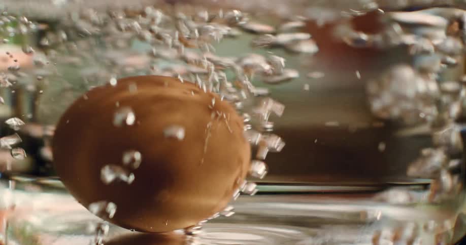 A brown egg is in a clear pot of boiling water as bubbles rise to the top