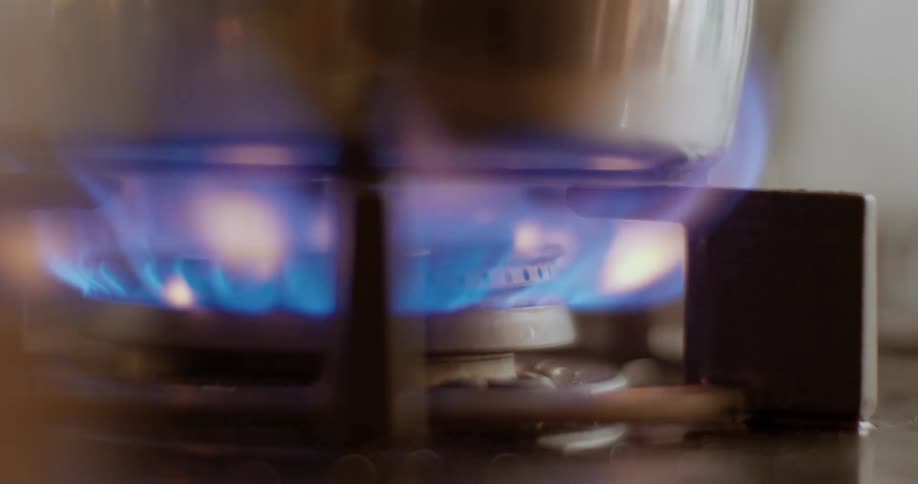 Close up of gas stove burning as a pot is placed on top,  in a kitchen