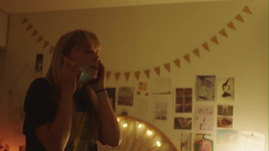 An upset girl at home walks around her room as she talks on the phone
