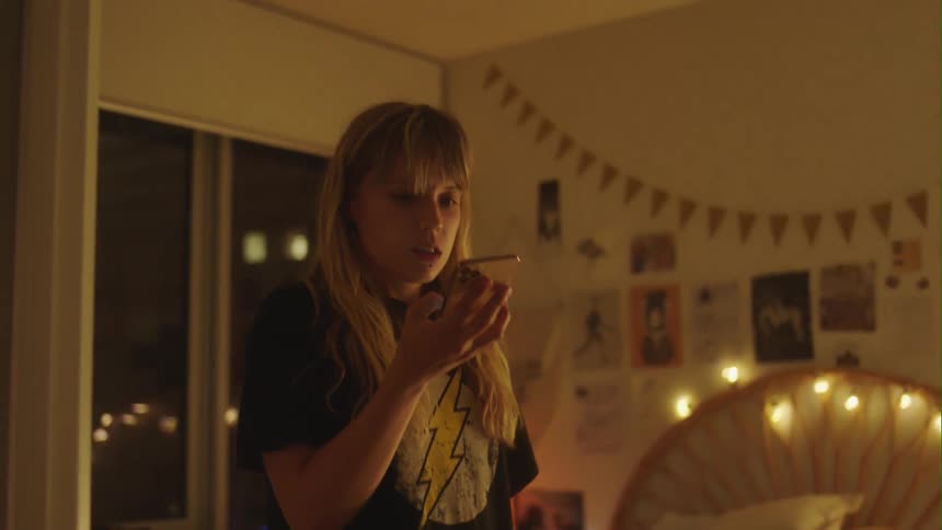 A worried looking girl holds her cell phone to her ear and then pulls it away and looks at it