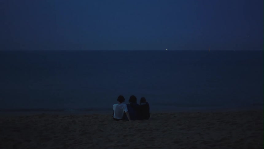 Three people sit on the beach at sunset