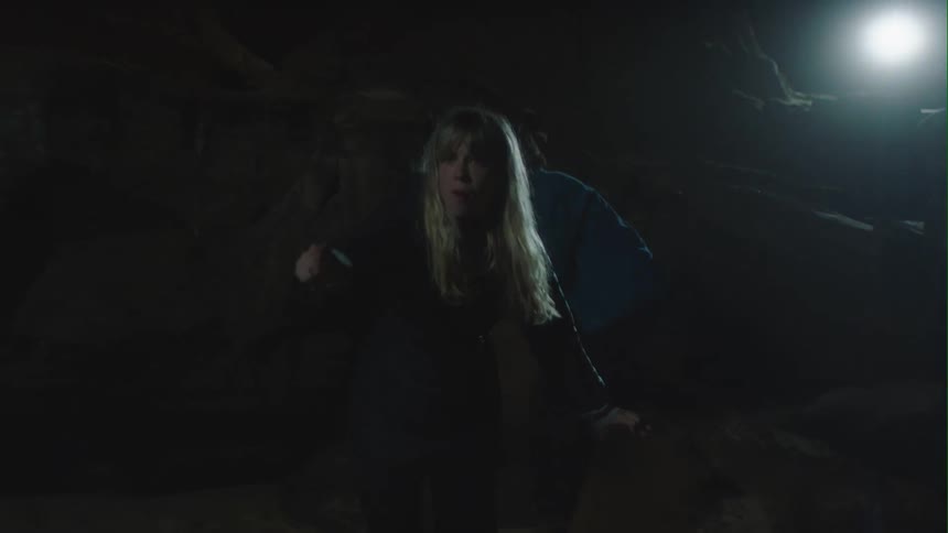 Woman yells and runs toward someone as she and man clamber over boulders at night
