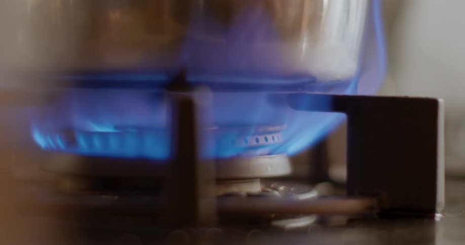 A cooking pot is place over the blue gas flames of a stove at home