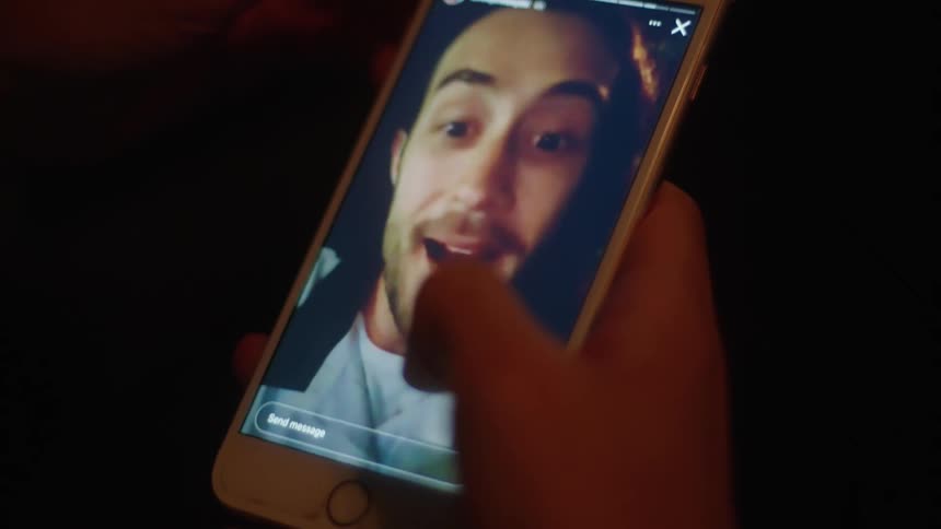 Someone is holding their phone as they watch a video of a man on the screen