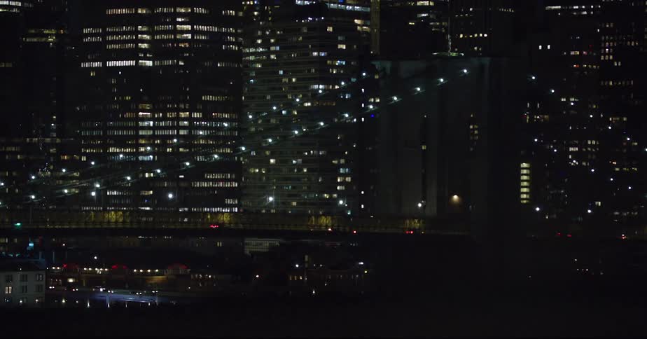Illimunated suspension bridge against the high rise buildings at night