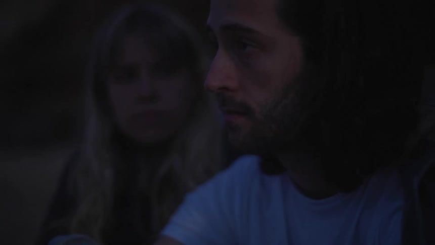 Blonde woman holds sad mans arm wearing white t shirt at dusk