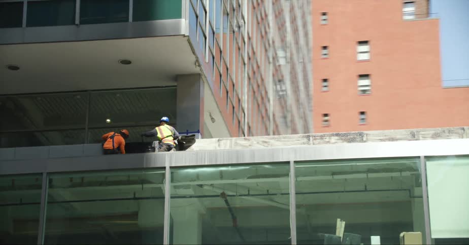 Two construction workers work on roof of building in downtown