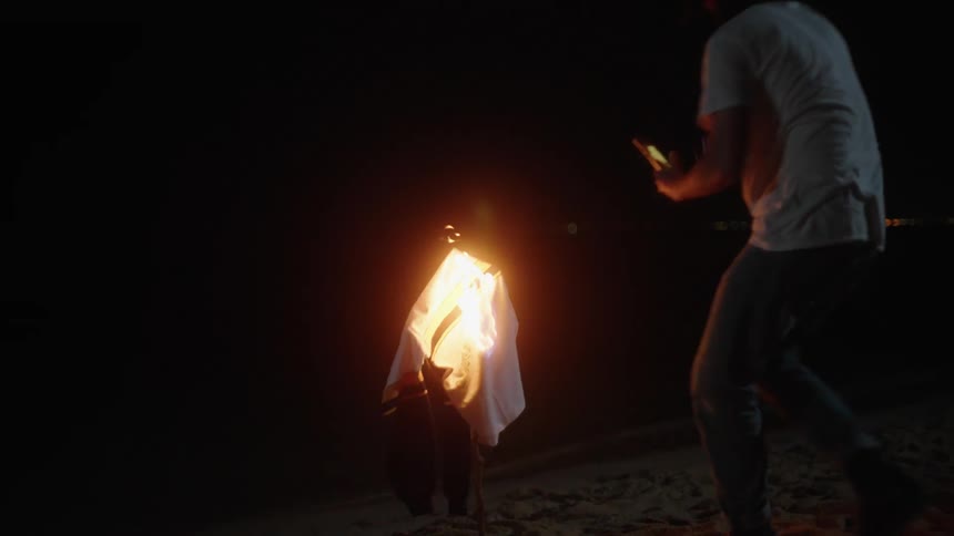 A man lights a shirt on fire at the beach