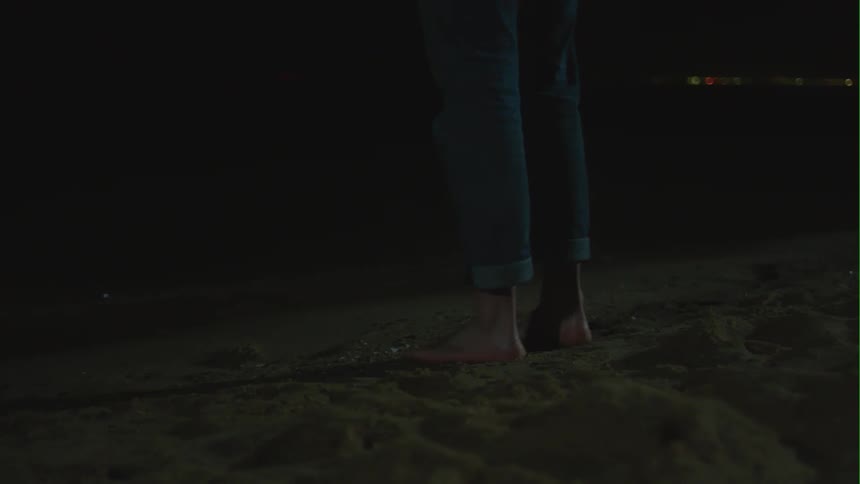 A person standing barefoot on a sandy beach at night