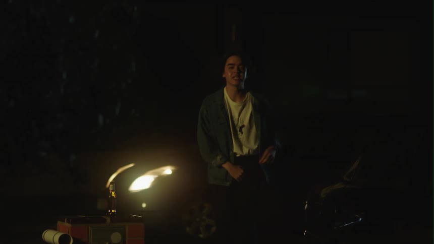 Young man drinking beer outdoors at night waiths uncomfortably for a friend to pick him up in a car