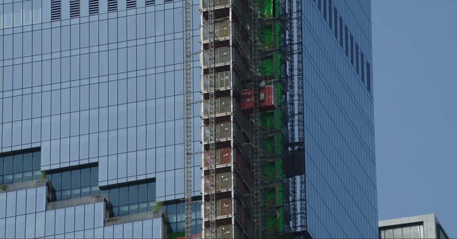A construction elevator slowly descends down the side of a tall building