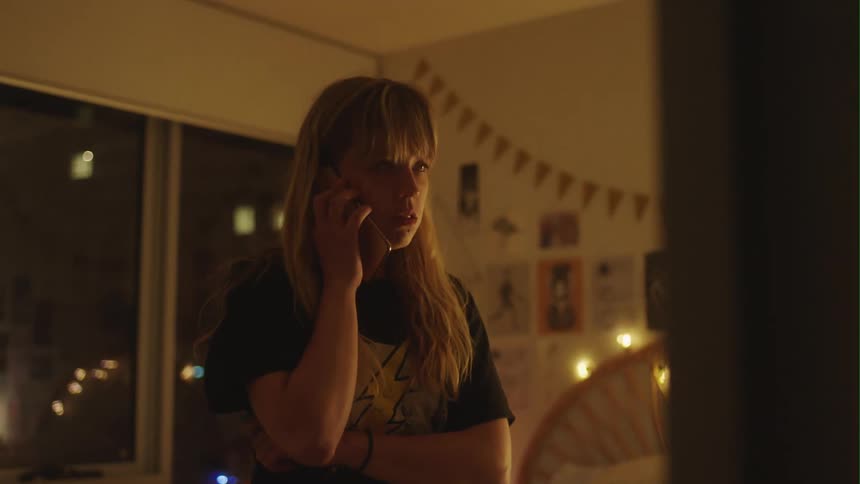 Agitated woman waits while listening to phone near sliding glass doors showing night