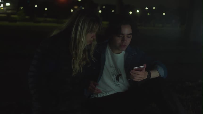 Man and woman sitting on ground using smartphone get up and runs away in street at night