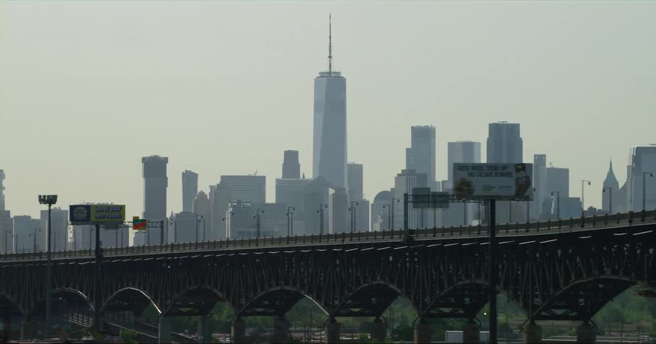 Tall downtown buildings and towers stand behind a highway bridge under a hazy sky