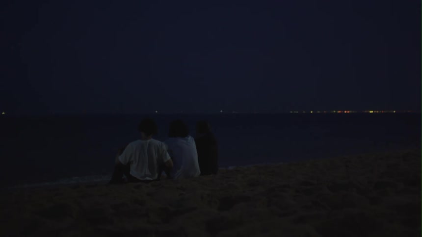 A group of friends embrace while sitting on the beach at night