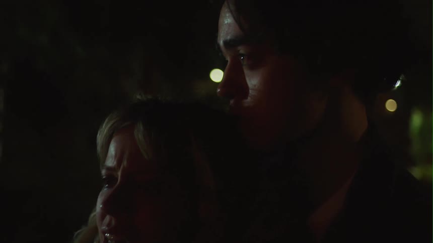 A man and a woman are standing together in the darkness and they look sad and she is crying