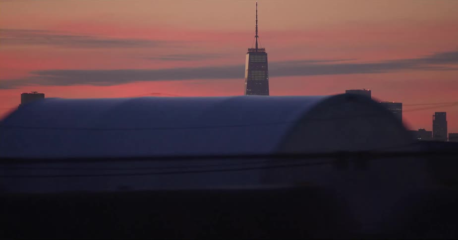 City skyscraper with spire seen from vehicle driving on highway at dusk