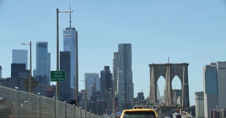 Cars traveling over a large city bridge with skyscrapers in the distance