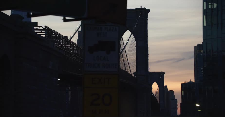 The silhouette of the brooklyn bridge with cable lights glowing and flag blowing