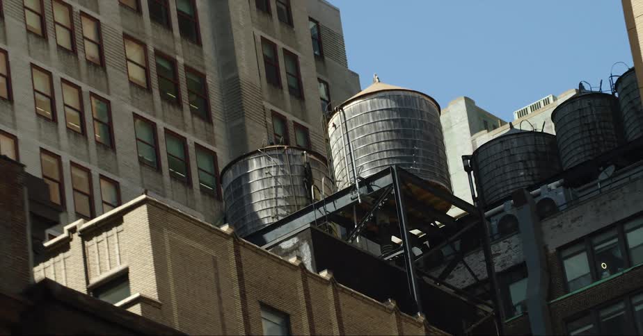 Rooftop water towers on city buildings under a bright blue sky
