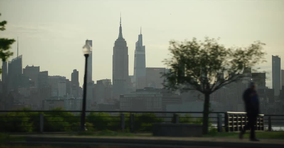 A person walking through an urban park with skyscrapers in the distance at dawn