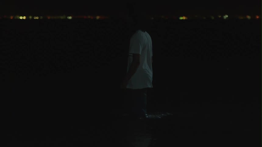 Young man fully clothed in a beach at night slowly walks into the ocean