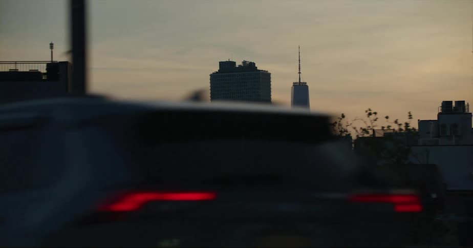 Cars traveling on a city road with skyscrapers in the distance at sunset