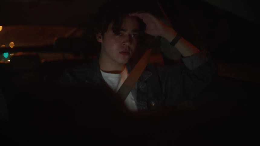 Sad man with denim jacket and white shirt drives car on highway at night crying