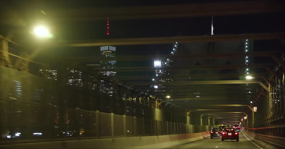 Traffic moves across a bridge into downtown at night and the city skyline is lit up brightly in the darkness