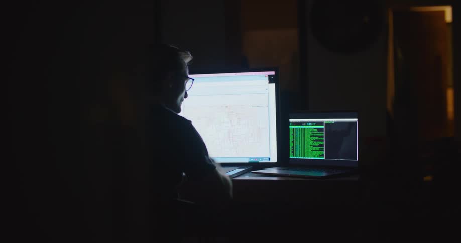 A man sits in a dark office and works on a laptop