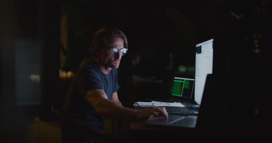 A man sits at a desk with a laptop and large computer screen in front of him