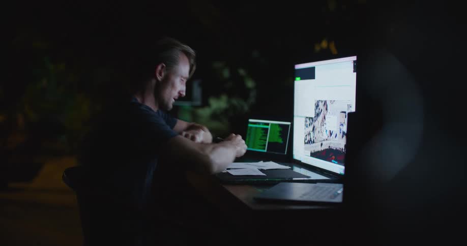 Man takes his eyeglasses off and rubs his eyes while working at night in dark room