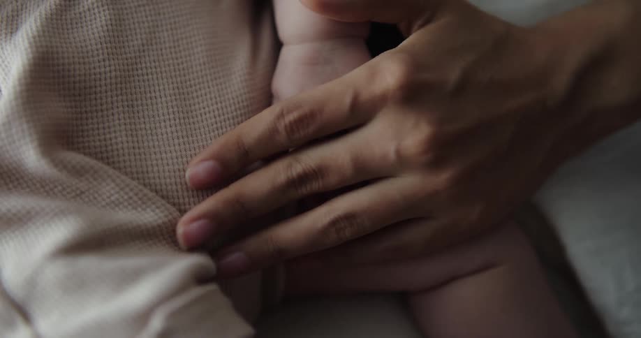 Woman holds child close and strokes the childs arm with a hand