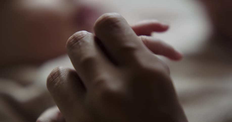 An adult holds and caresses that hand of a small resting child