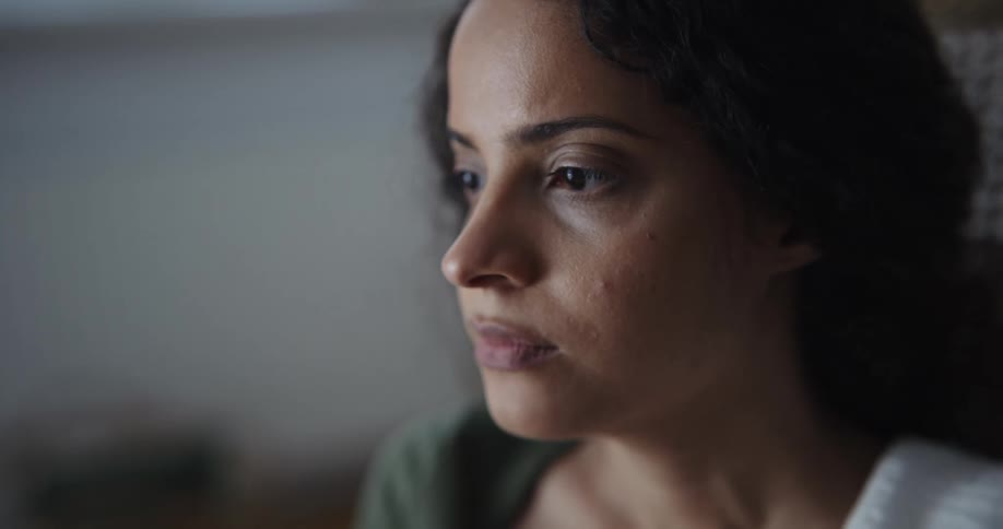 Close up of the face of a woman sitting on a rocking chair inside a room