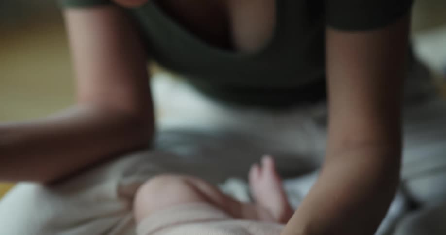 A woman is lying down and holding the hands of her baby and smiling and talking