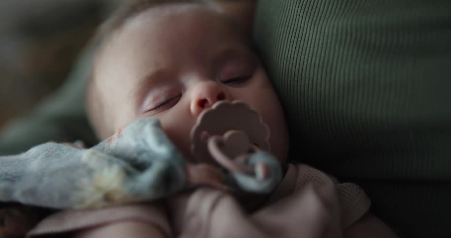 A baby sleeps on the couch with a pacifier