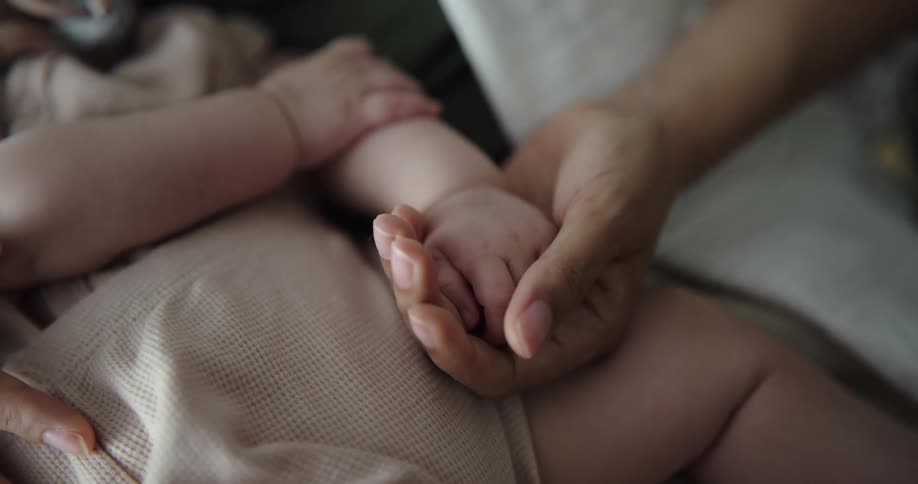 A woman caresses her babys hand while they nap