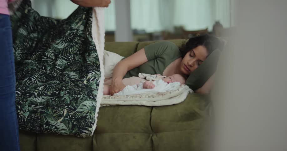 Woman walks into room with a blanket that she places over sleeping mother and her baby
