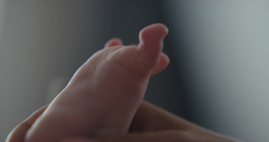 A baby moves their toes as the mother holds their foot