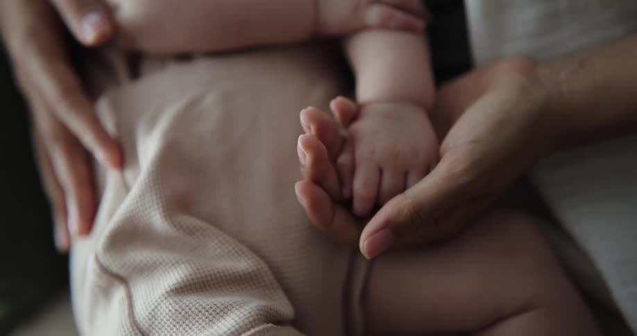 A woman holds her baby son and caresses his hand