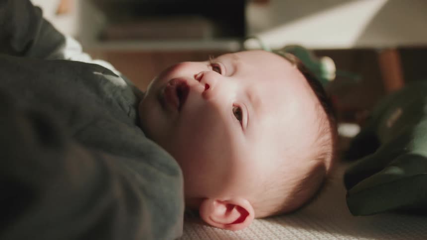 Light shines on face of baby lying on bed near toys